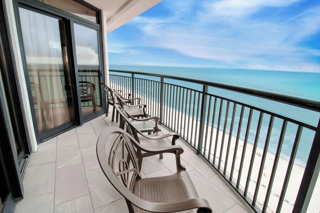 Expedia A spacious balcony outdoor lounge chairs, bright blue ocean and white sand beach under a partly cloudy sky.