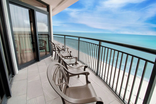 Expedia A spacious balcony outdoor lounge chairs, bright blue ocean and white sand beach under a partly cloudy sky.